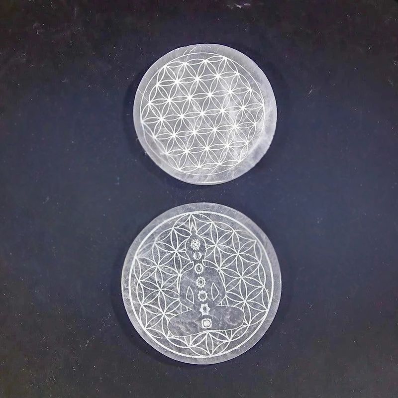 Plaques de rechargement en Sélénite Fleur de vie de 10cm avec motifs gravés distincts, superposées sur fond noir.