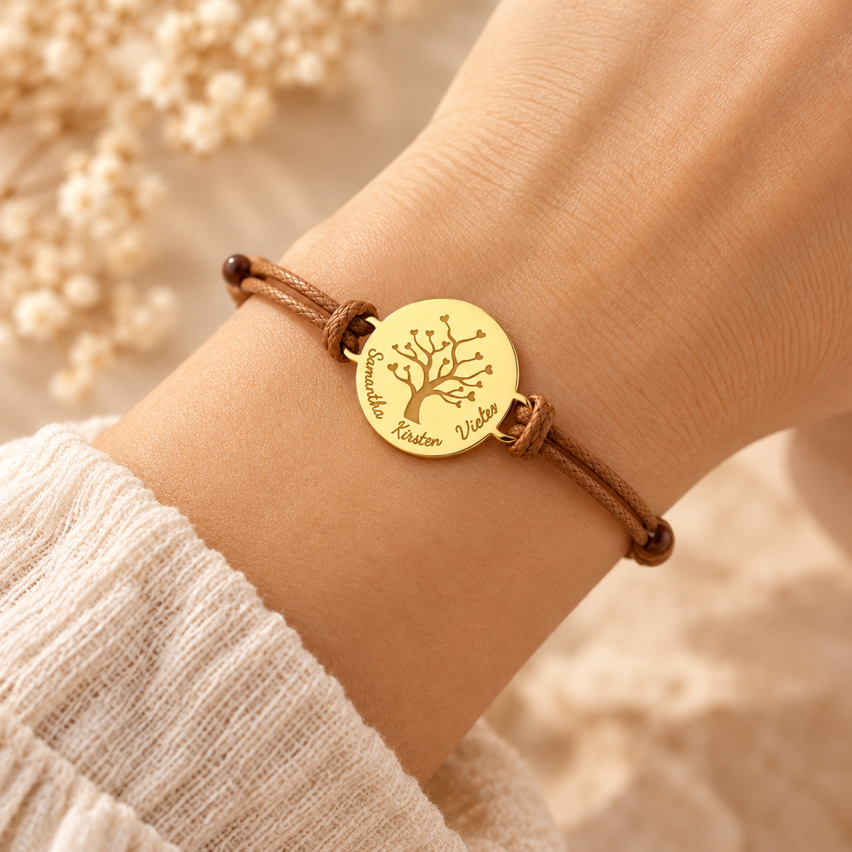 Bracelet arbre de vie personnalisé doré porté au poignet d'une femme, avec gravure de prénoms et cordon marron