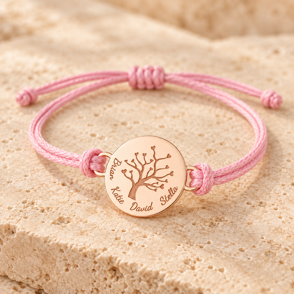 Bracelet arbre de vie personnalisé or rose avec cordon rose ajustable et médaille gravée de prénoms sur fond beige