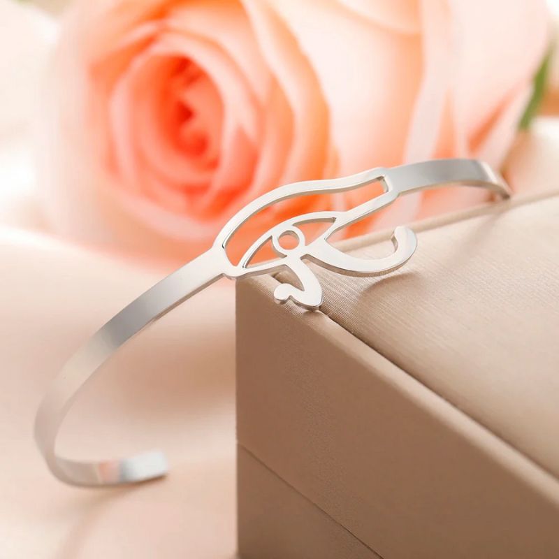 Bracelet Oeil d'Horus en argent reposant sur une boîte à bijoux, avec une rose en arrière-plan.