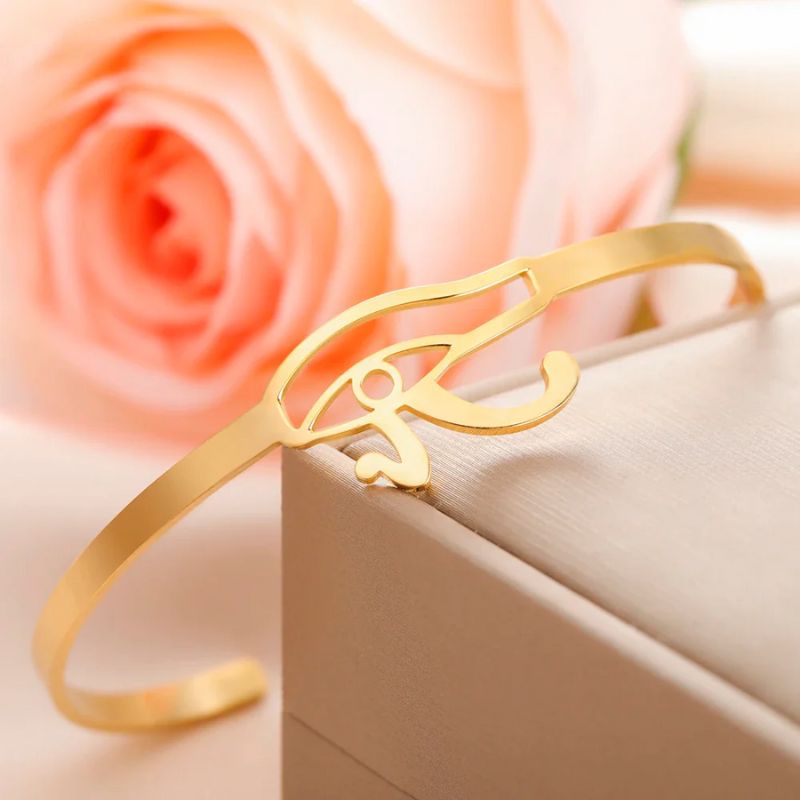 Bracelet Oeil d'Horus en or délicatement posé sur une boîte à bijoux, accompagné d'une rose.