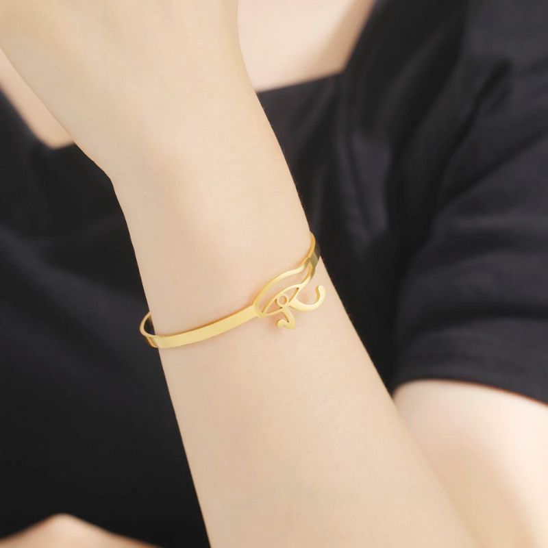 Bracelet Oeil d'Horus en or porté au poignet d'une femme vêtue de noir.