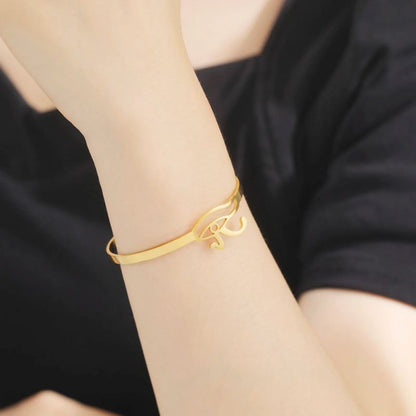 Bracelet Oeil d'Horus en or porté au poignet d'une femme vêtue de noir.