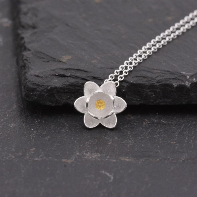 Zoom sur la Fleur de Lotus en argent avec cœur or, bijou délicat mis en scène sur ardoise noire