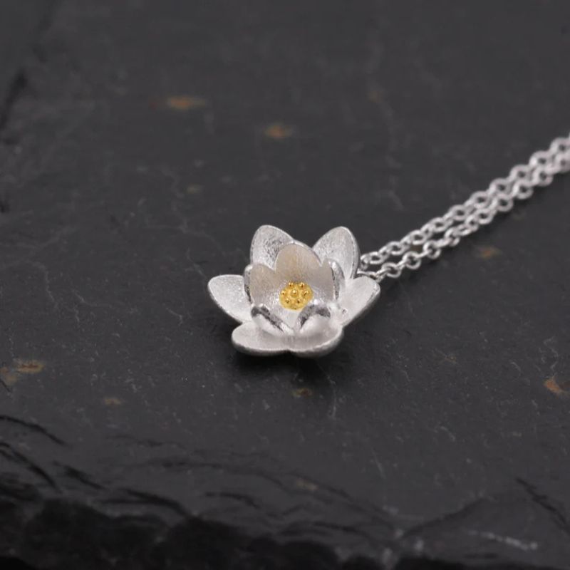 Détail du pendentif en forme de Fleur de Lotus en argent avec cœur or, mis en valeur sur fond noir texturé