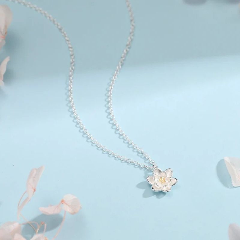 Collier Fleur de Lotus en argent sur fond bleu avec ambiance poétique, chaîne fine et pendentif en forme de fleur délicate