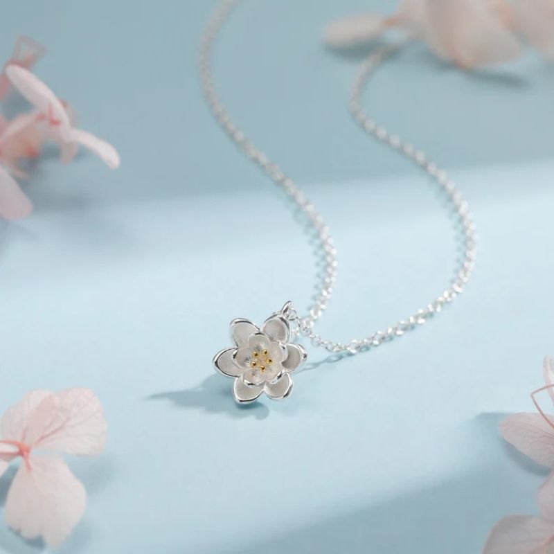 Collier Fleur de Lotus en argent sur fond bleu avec fleurs séchées, ambiance poétique et douce