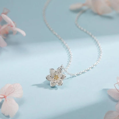 Collier Fleur de Lotus en argent sur fond bleu avec fleurs séchées, ambiance poétique et douce