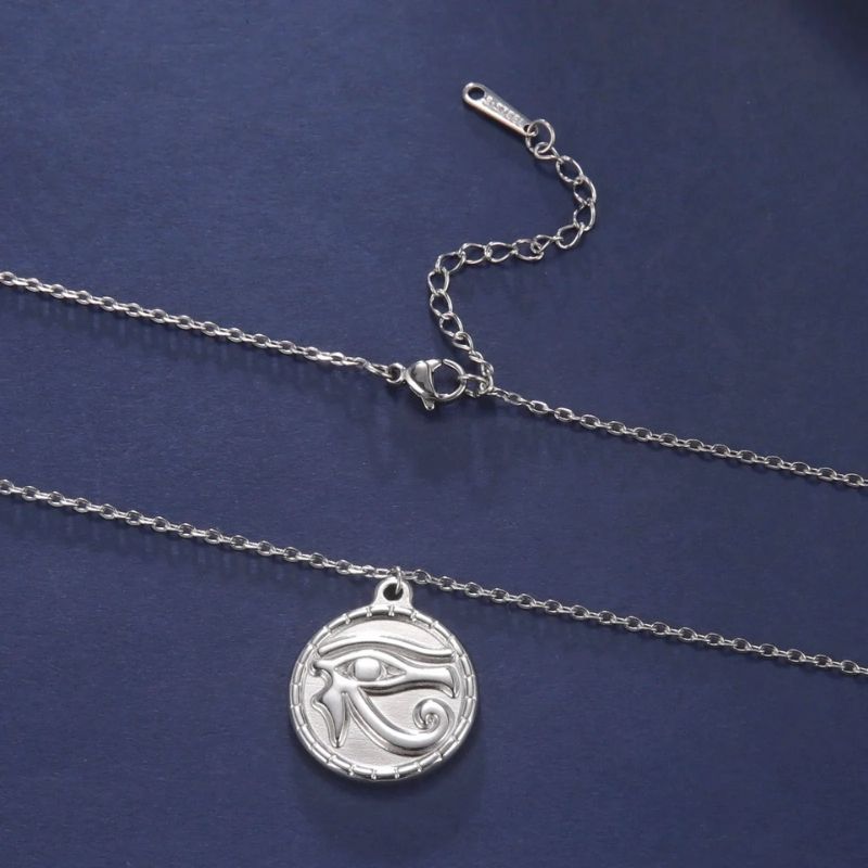Pendentif Œil d'Horus en acier inoxydable argenté, posé sur un fond bleu avec sa chaîne ajustable, idéal pour une touche élégante et spirituelle.
