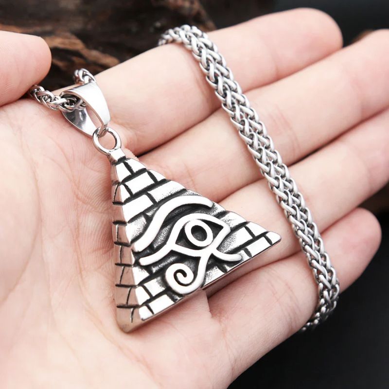 Pendentif Oeil d'Horus en argent tenu dans une main, illustrant sa taille et son motif en relief représentant une pyramide gravée.