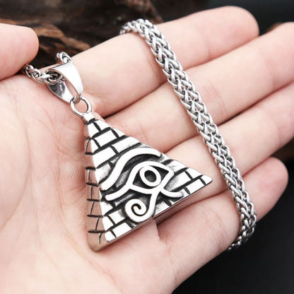 Pendentif Oeil d'Horus en argent tenu dans une main, illustrant sa taille et son motif en relief représentant une pyramide gravée.