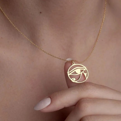 Pendentif Oeil d'Horus en or délicatement tenu entre les doigts d'une femme, illustrant son élégance et sa symbolique spirituelle.